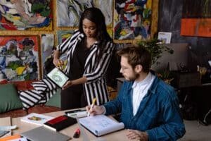 Two artists collaborating in a colorful art studio, sharing ideas and designs.